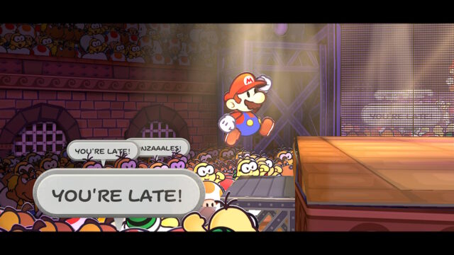 Screenshot of the game Paper Mario: The Thousand-Year Door. The screenshot shows The Great Gonzalez jumping onto the stage while the crowd jeers him on telling him he's late.