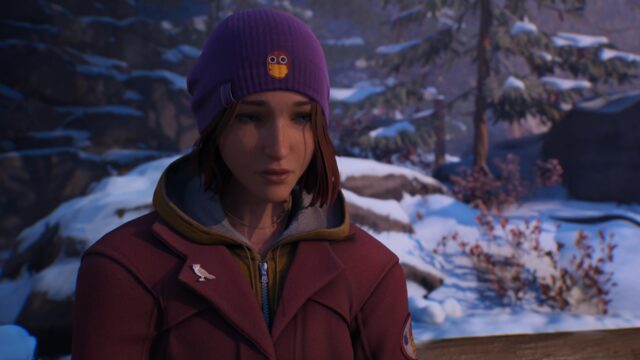 Screenshot from the game Life is Strange: Double Exposure. Max Caulfield is looking pensive in a cute purple beanie with a lil' hotdog cartoon character on the front and a red coat over a mustard yellow zip-up hooded sweatshirt.